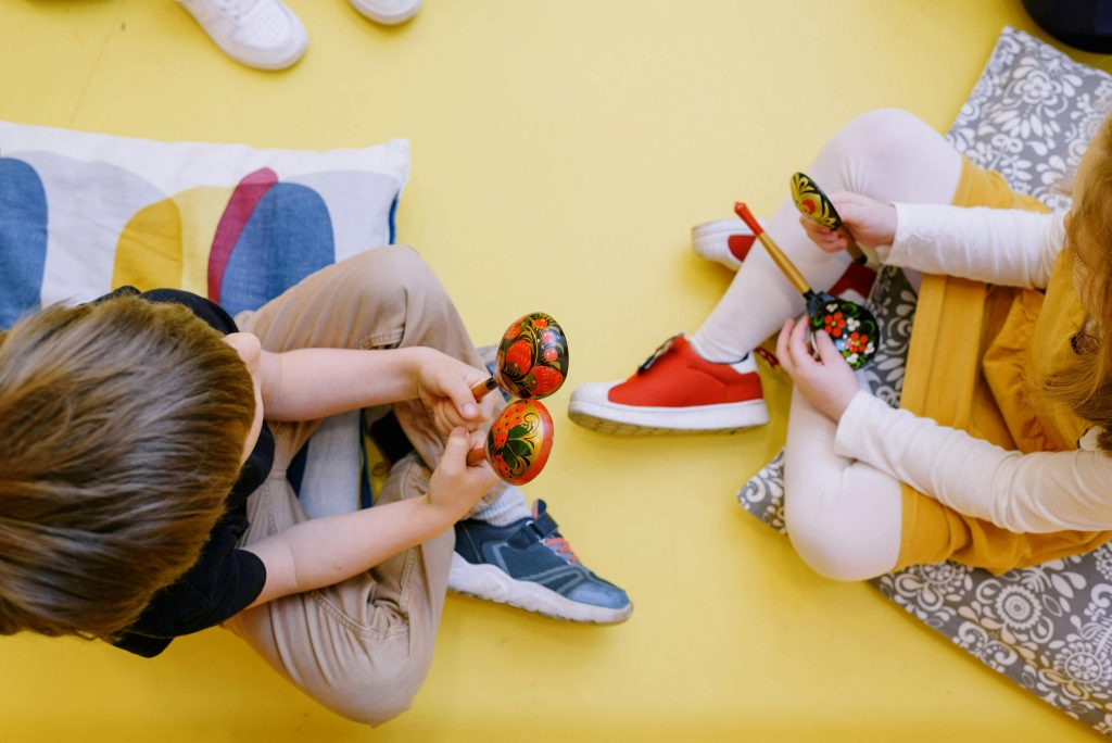 Musik, Bewegung & Spaß (2-3 Jahre) 1 Joyful children playing maracas in a colorful preschool setting.